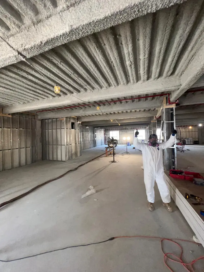 Installer in protective equipment beneath a spray-foamed commercial roof deck