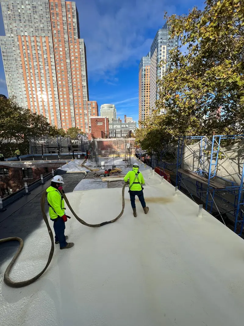 Two installers applying spray polyurethane foam across a commercial flat roof